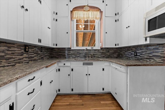 Kitchen with white appliances, white cabinetry, wood finished floors, stone counters, and tasteful backsplash | Image 15