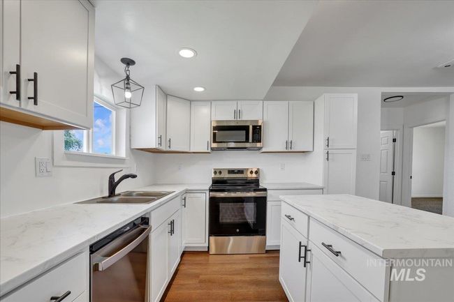 Kitchen featuring appliances with stainless steel finishes, white cabinets, decorative light fixtures, light stone counters, and recessed lighting | Image 8