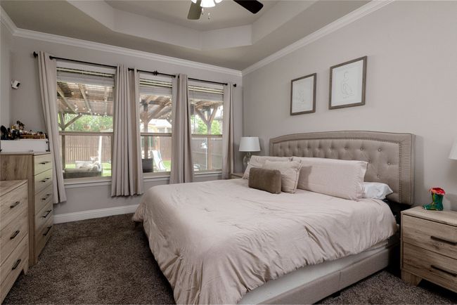 Primary bedroom featuring a tray ceiling, carpet, ceiling fan, baseboards, three large windows with window coverings and ornamental molding | Image 8