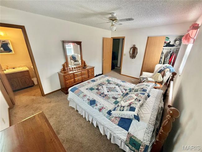 Bedroom featuring light colored carpet, a closet, a textured ceiling, ensuite bathroom, and a ceiling fan | Image 33