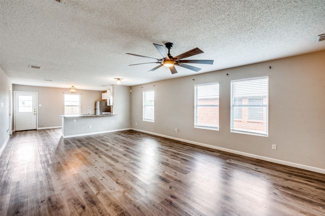 Unfurnished living room with a ceiling fan, a textured ceiling, wood finished floors, and baseboards | Image 5