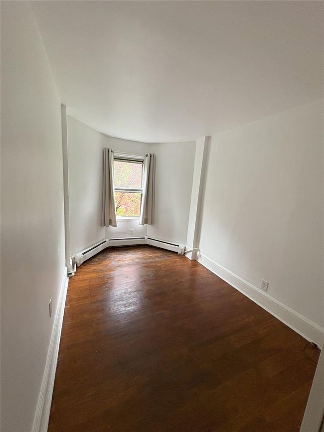 Unfurnished room featuring dark wood-style floors, baseboards, and a baseboard heating unit | Image 7