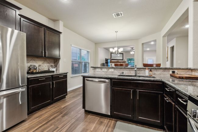 Kitchen featuring stainless steel appliances, a sink, backsplash, stone countertops, and wood finished floors | Image 8