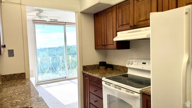 Kitchen with white appliances, carpet flooring, under cabinet range hood, dark countertops, and ceiling fan | Image 31