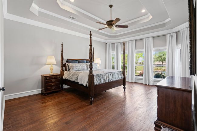 Bedroom with a tray ceiling, dark wood-style flooring, ornamental molding, and visible vents | Image 24