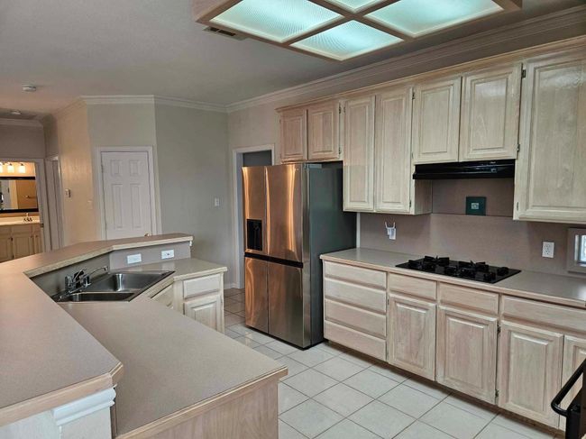 Kitchen with black gas stovetop, stainless steel refrigerator with ice dispenser, crown molding, light tile patterned floors, and light countertops | Image 21