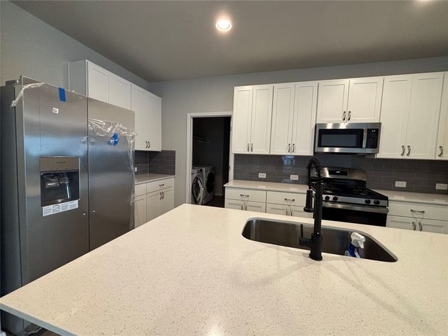 Kitchen featuring appliances with stainless steel finishes, washer and dryer, tasteful backsplash, white cabinets, and recessed lighting | Image 7