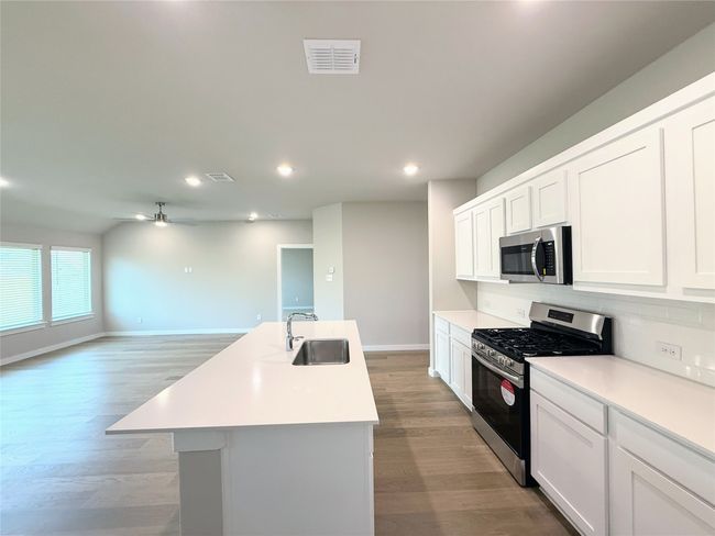Kitchen featuring stainless steel appliances, decorative backsplash, ceiling fan, light wood-style floors, and light countertops | Image 8