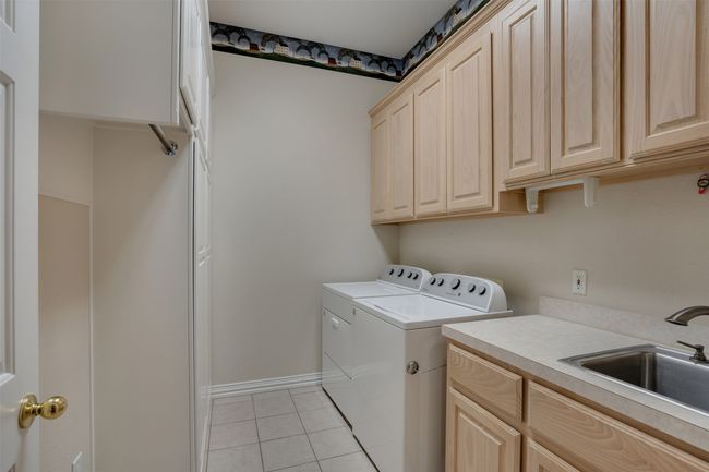 Washroom featuring washing machine and dryer, cabinet space, light tile patterned floors, and baseboards | Image 31