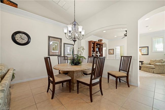 Dining room with crown molding, light tile patterned flooring, arched walkways, ceiling fan with notable chandelier, and lofted ceiling | Image 12