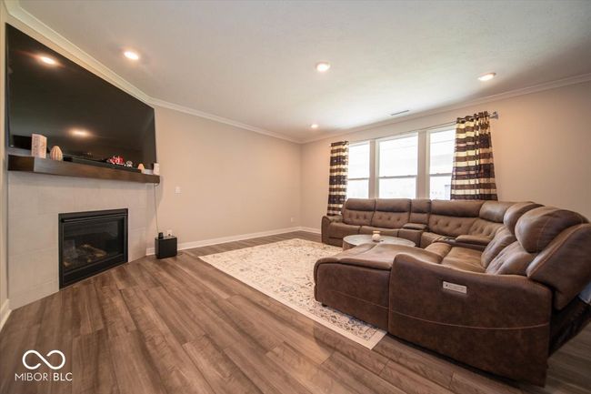 living room featuring wood finished floors, a tile fireplace, crown molding, and recessed lighting | Image 7