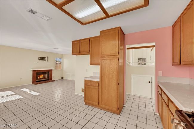 Kitchen with tile countertops, light tile patterned floors, visible vents, stove, and open floor plan | Image 9