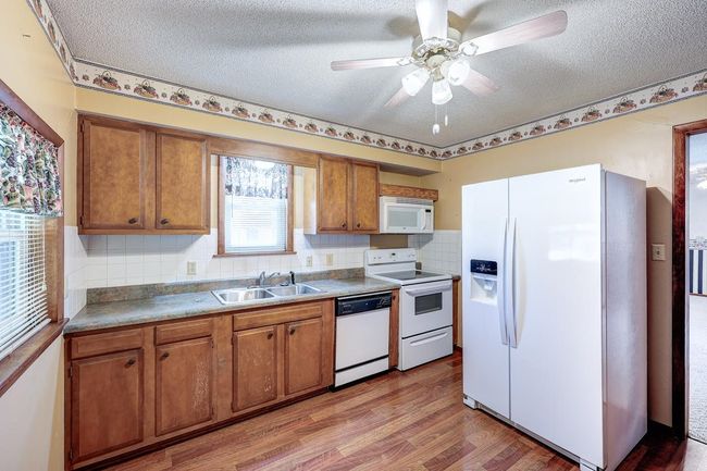Kitchen featuring white appliances, a sink, brown cabinets, a textured ceiling, and light wood-style floors | Image 4
