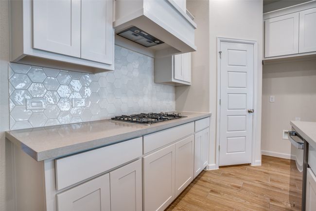 Kitchen featuring custom range hood, light wood-style floors, decorative backsplash, appliances with stainless steel finishes, and light countertops | Image 11