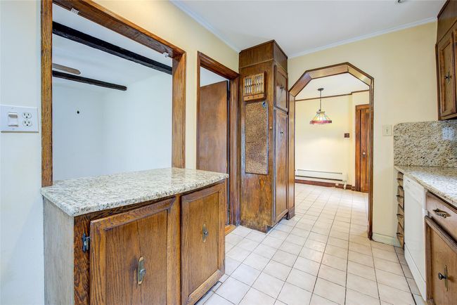 Kitchen featuring baseboard heating, light tile patterned floors, crown molding, light stone counters, and decorative light fixtures | Image 12