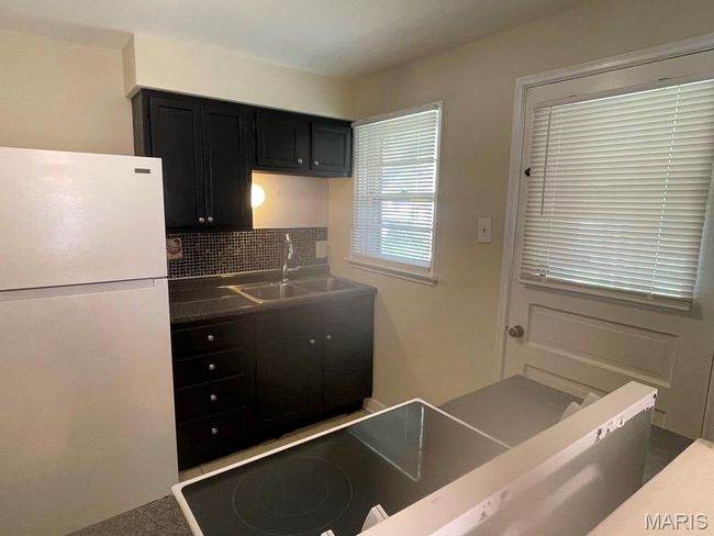 Kitchen with a sink, dark countertops, freestanding refrigerator, decorative backsplash, and dark cabinets | Image 12