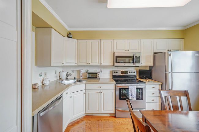 Kitchen featuring stainless steel appliances, white cabinetry, crown molding, light wood-style floors, and decorative backsplash | Image 7