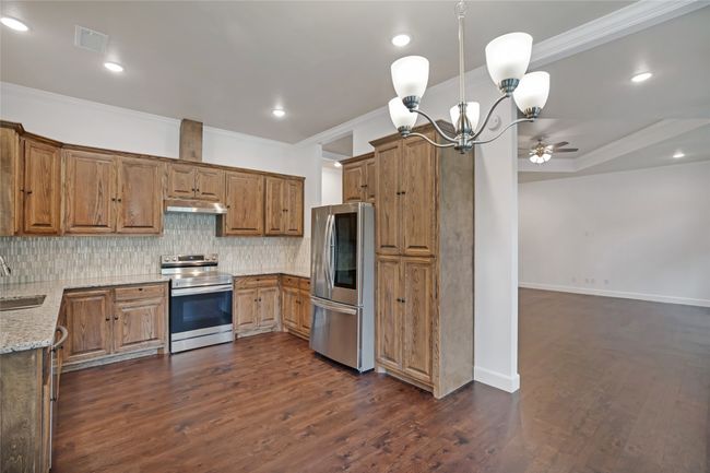 Kitchen with stainless steel appliances, under cabinet range hood, crown molding, light stone counters, and decorative backsplash | Image 28