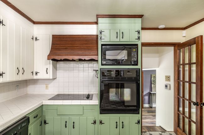 The kitchen has tile countertops and back splash along with a cooktop and built in oven. | Image 26