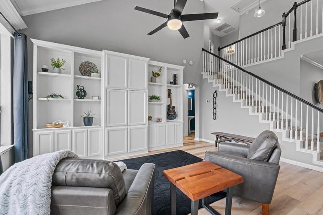 Living area featuring ceiling fan, high vaulted ceiling, light wood-style floors, stairs, and ornamental molding | Image 9