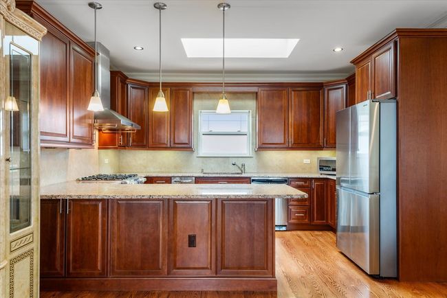 Kitchen featuring a skylight, appliances with stainless steel finishes, a peninsula, wall chimney range hood, and a sink | Image 4