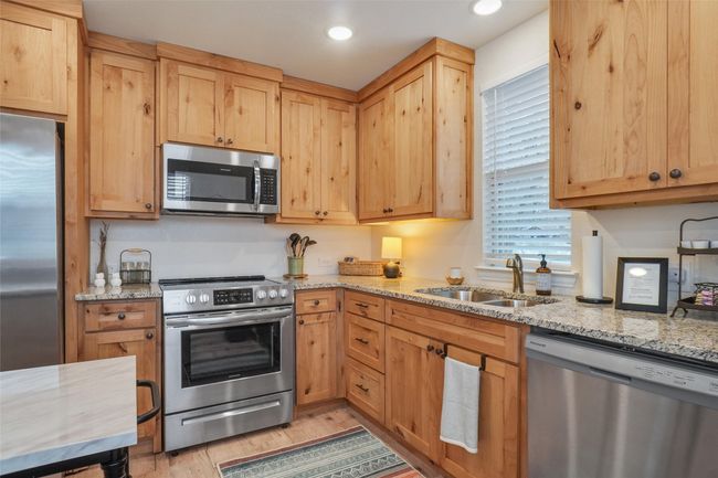 Kitchen with appliances with stainless steel finishes, light brown cabinetry, sink, light stone counters, and light hardwood / wood-style floors | Image 7