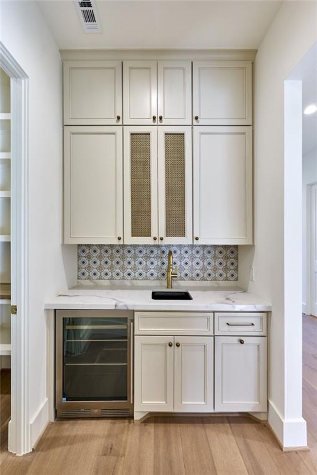 Showcasing a stylish wet bar with decorative tile backsplash, and a built-in wine cooler. | Image 24