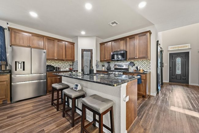 Kitchen featuring appliances with stainless steel finishes, decorative backsplash, a kitchen breakfast bar, dark wood-style floors, and recessed lighting | Image 8