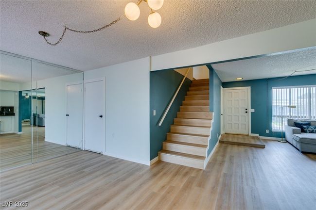 Unfurnished living room featuring a textured ceiling, light wood-type flooring, stairs, and a chandelier | Image 15