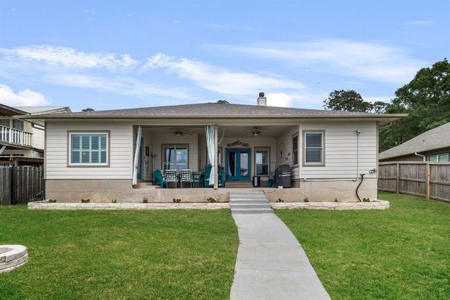 This is a charming single-story home featuring a spacious covered back patio with seating, perfect for outdoor relaxation. It has a well-maintained lawn and is bordered by a wooden fence for added privacy. | Image 27