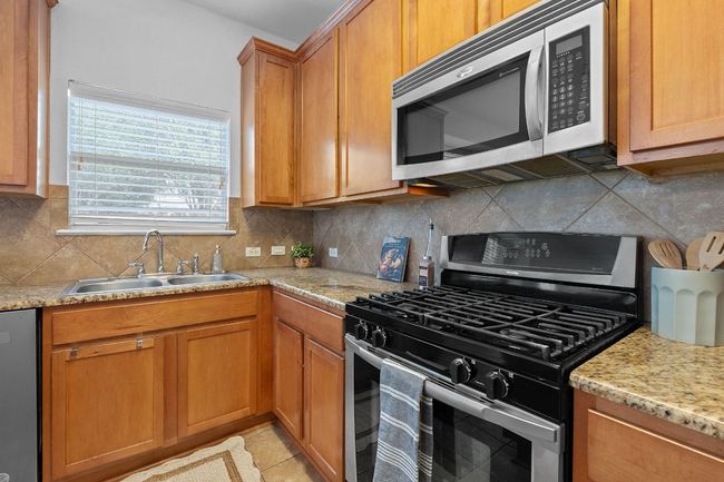 Kitchen featuring stainless steel appliances, a sink, tasteful backsplash, brown cabinetry, and light stone countertops | Image 9