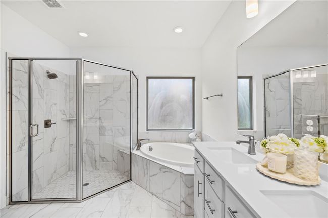 Primary bathroom features a modern design with a glass-enclosed shower, a soaking tub, and a double vanity. | Image 18