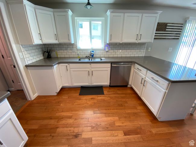 Kitchen featuring stainless steel dishwasher, a sink, a peninsula, light wood-style flooring, and white cabinetry | Image 9