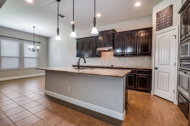 Kitchen with tile patterned floors, tasteful backsplash, a kitchen island with sink, light stone countertops, and recessed lighting | Image 10