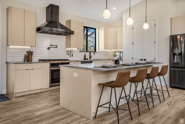 Kitchen featuring wall chimney range hood, a center island, appliances with stainless steel finishes, and light wood finished floors | Image 6