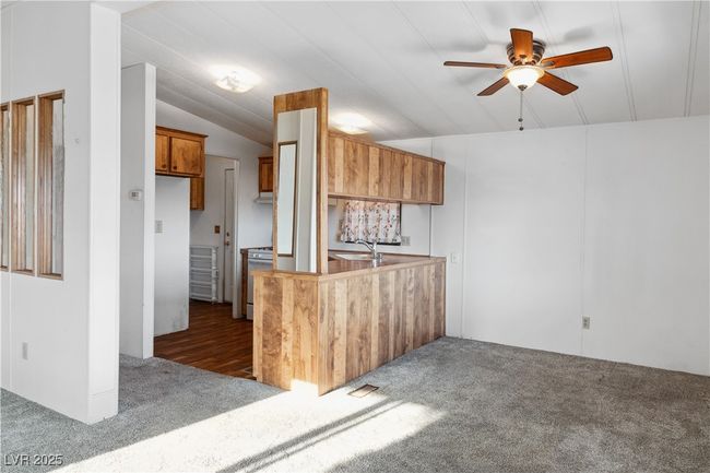 Dining area with breakfast bar/passthrough window to Kitchen with wood cabinetry, lofted ceiling, dark carpet, and gas stove | Image 10