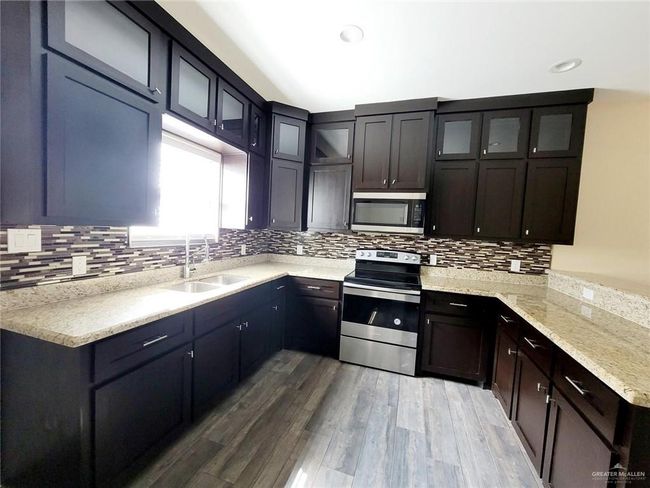 Kitchen with stainless steel appliances, backsplash, wood finished floors, glass insert cabinets, and recessed lighting | Image 6
