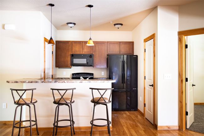 Kitchen with black appliances, a breakfast bar area, light wood-type flooring, brown cabinetry, and pendant lighting | Image 11