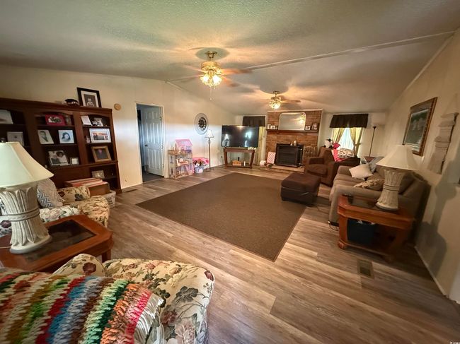 Living area featuring ceiling fan, lofted ceiling, a large fireplace, wood finished floors, and a textured ceiling | Image 5