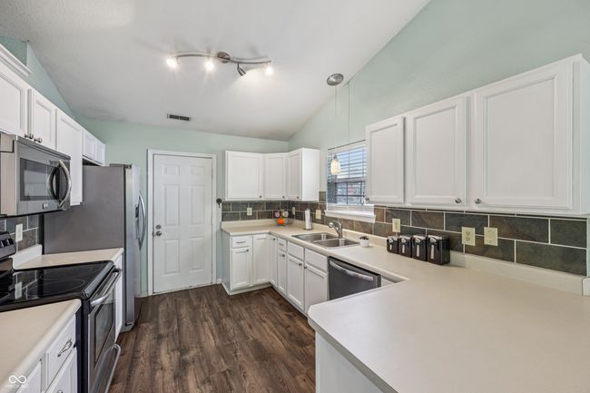 kitchen with appliances with stainless steel finishes, tasteful backsplash, white cabinets, dark wood finished floors, and light countertops | Image 12