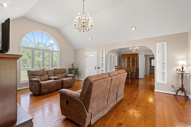 Living room with arched walkways, a chandelier, lofted ceiling, built in features, and wood finished floors | Image 8