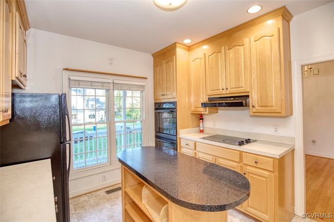 Kitchen with light brown cabinets, open shelves, black appliances, under cabinet range hood, and visible vents | Image 10