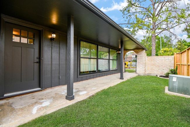 This photo showcases a charming covered porch with a modern dark exterior and large windows, leading to a private fenced yard with lush green grass and a brick wall, perfect for outdoor relaxation. | Image 45