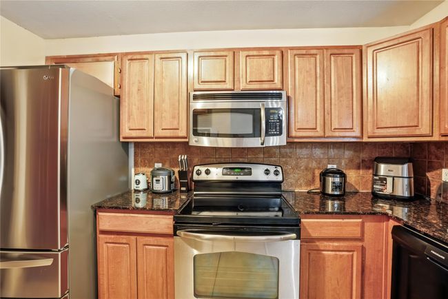 Kitchen featuring stainless steel appliances, decorative backsplash, and dark stone countertops | Image 14