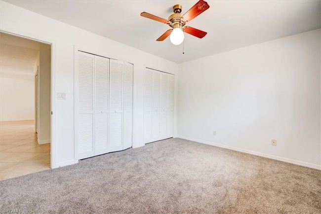 Unfurnished bedroom with carpet flooring, ceiling fan, baseboards, tile patterned floors, and multiple closets | Image 19