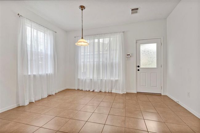 The breakfast room is bright with large windows, sheer curtains, and tiled flooring. Features a hanging light fixture and a door with frosted glass leading to the backyard. | Image 21