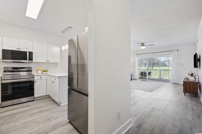 Kitchen featuring stainless steel appliances, light wood-type flooring, light countertops, and white cabinets | Image 11
