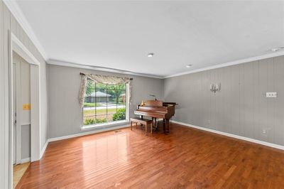 Empty room with light wood-type flooring, wood walls, and crown molding | Image 3