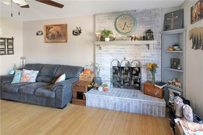 Living room featuring ceiling fan, hardwood / wood-style flooring, built in features, and a brick fireplace | Image 2