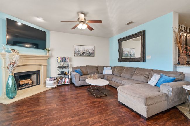 Living area with a fireplace with raised hearth, ceiling fan, dark wood-type flooring, and visible vents | Image 7